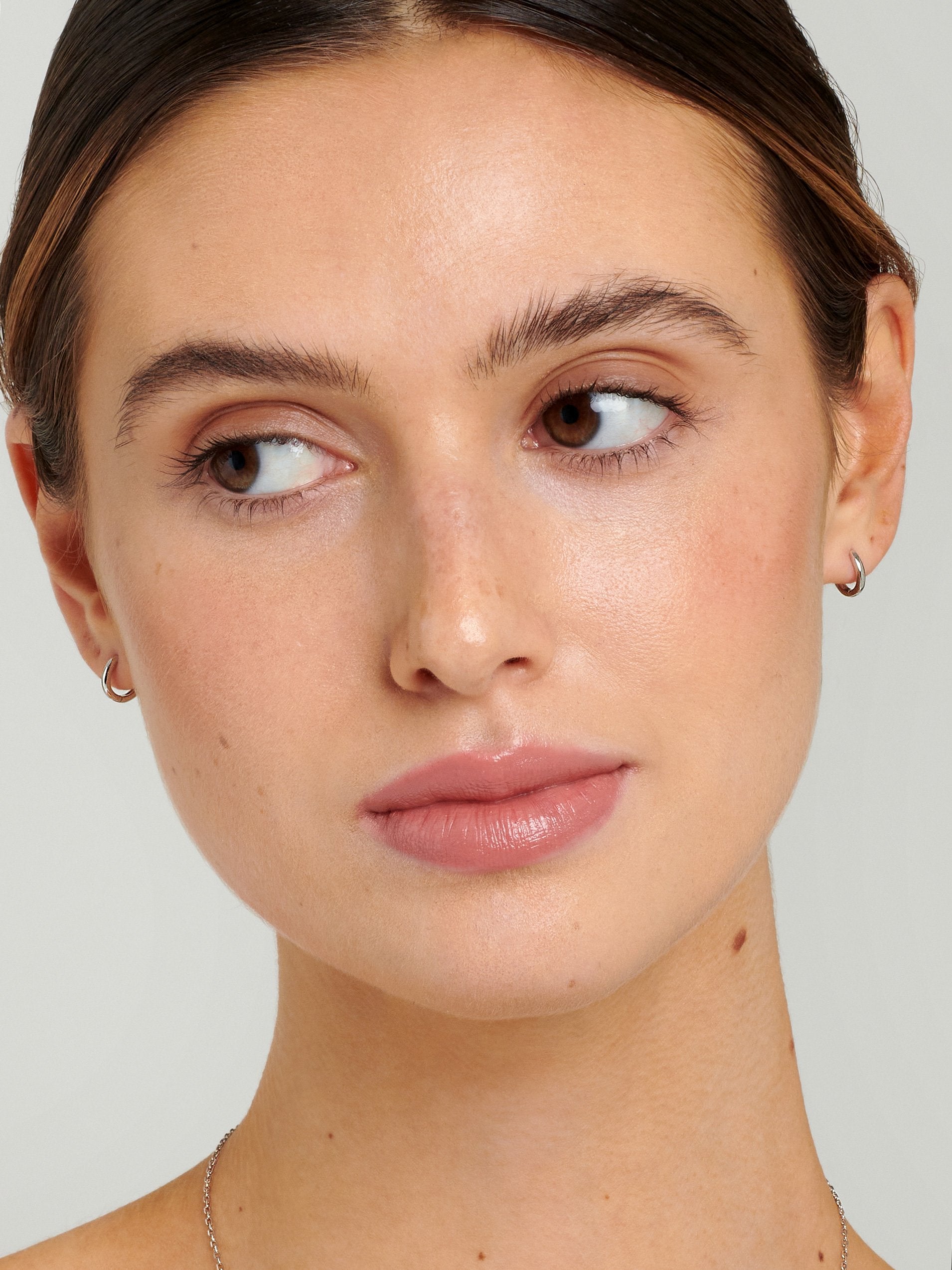 Model wearing tiny silver huggie hoops handcrafted from 18ct white gold plated sterling silver.