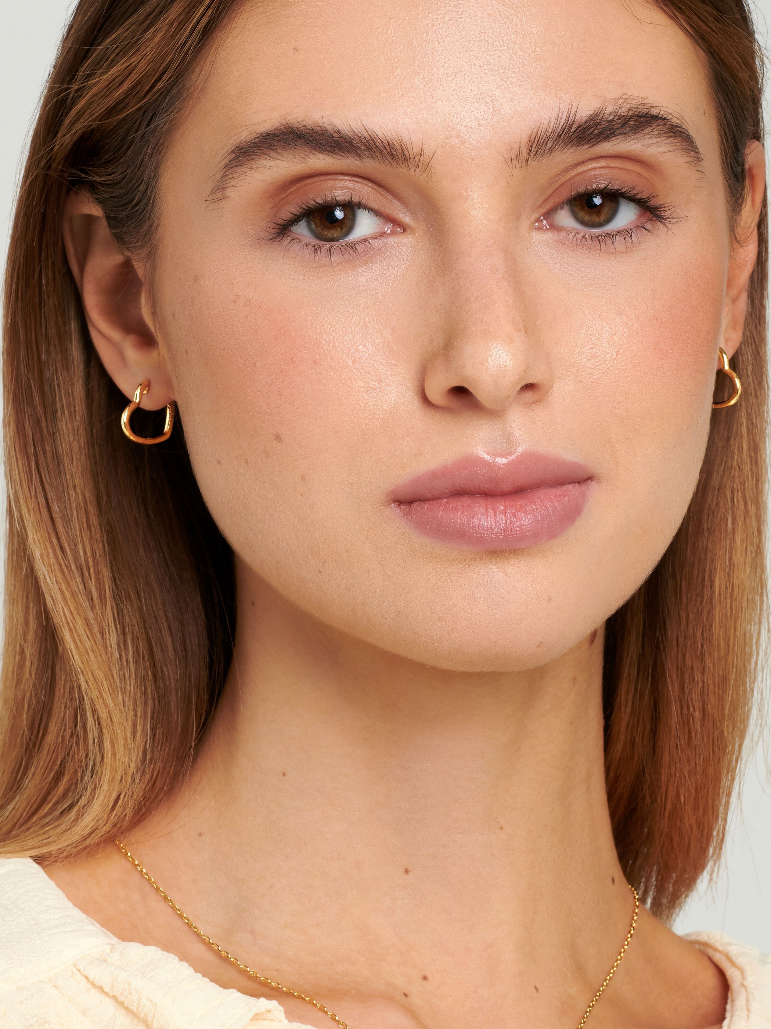 Female model with brown hair wearing gold heart hoop earrings.